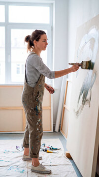Focused artist sweeps broad brushstroke of gray paint across large canvas