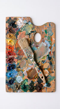Well worn palette displays layered oil colors beneath crossed painting brush