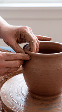 Steady hands raise tall clay vessel from wheel with careful precision skill