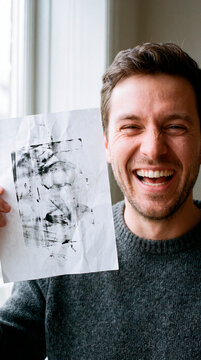 Delighted printmaker holds fresh abstract ink print near bright window