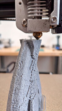 3D printer extrudes textured gray filament shaping twisted vertical form
