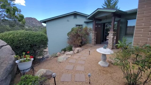 Sunlit outdoor patio beside blue house, umbrella shaded table chairs, stone tile terrace, mountains