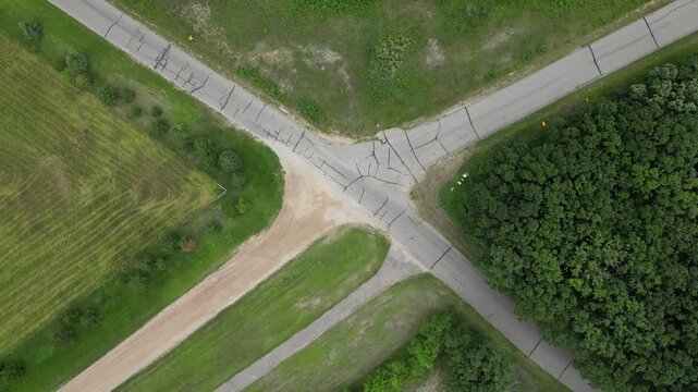 Countryside Crossroads. The meeting of decaying pavement and unpaved dirt roads, intersecting forest, pasture, grassland, and farm field. Rotating aerial done footage in rural America
