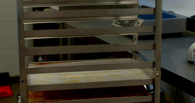 frontal view of metal bakery storage rack with repeating rails, mostly empty upper shelves, and one lower tray with light residue under cool neutral lighting, with