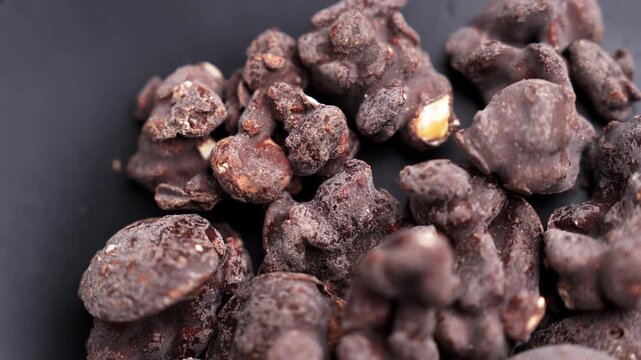 Delicious premium chocolate clusters with crunchy nuts and cookie pieces coated on dark ceramic surface