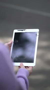 Close-up of a woman holding a damaged tablet with a shattered screen, representing broken technology, electronics failure, repair and consumer problems.
