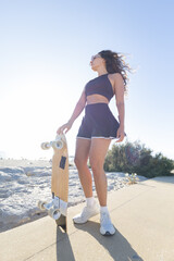 Skateboarding at the beach on a sunny day with a young woman holding a skateboard © KONSTANTIN SHISHKIN