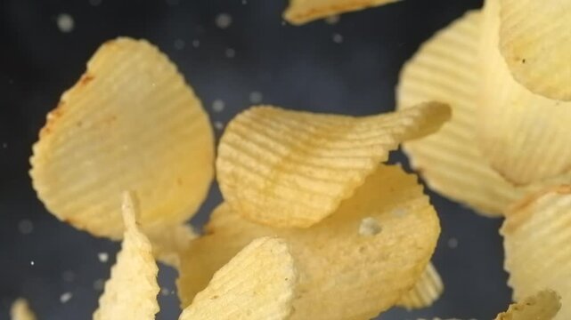 Ridged potato chips falling in slow motion on black background