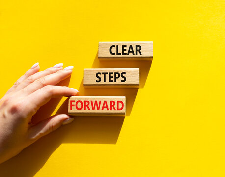 Concept words clear steps forward on wooden blocks arranged as steps. Businessman hand arranging wooden blocks. Progress and planning concept. Yellow background. Copy space.