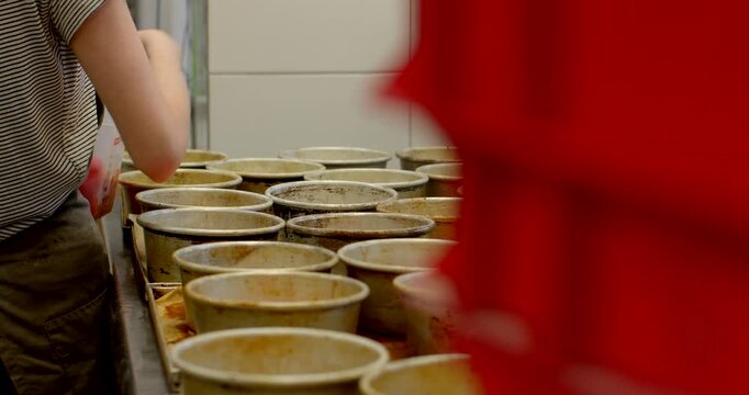 forearm and hand of bakery worker reaching into grid of round, used metal baking tins on stainless steel counter inside commercial kitchen, tins show baked residue