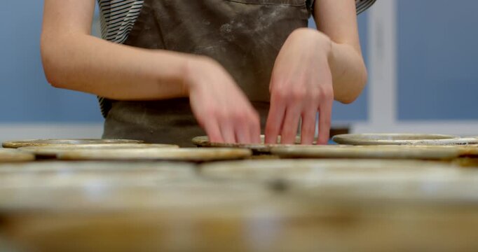close-up showing baker hands placing dough portions into metal baking tins on bakery counter, flour dust and worn tin texture visible as fingers press and arrange