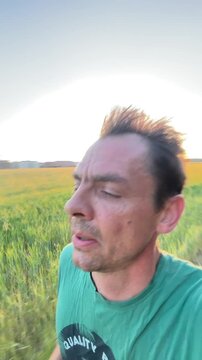 close-up of adult man running beside expansive golden-green crop field at sunset, face flushed and hair tousled with low sun behind creating bright backlight halo
