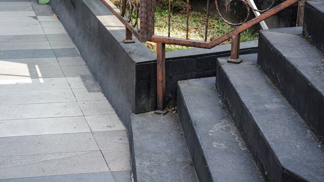 Exterior black granite staircase with a ornamental iron guardrail along a paved walkway on a sunny day.