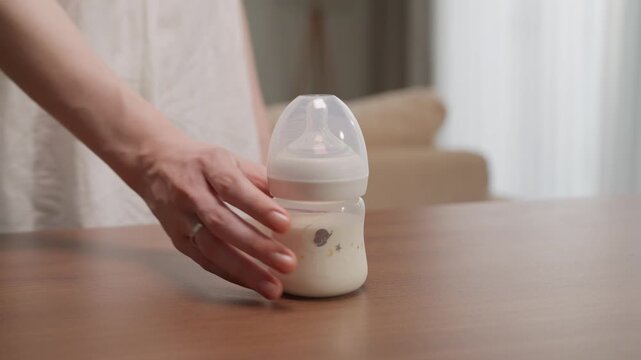 Mother Hand Reaching for a Baby Milk Bottle on a Wooden Table