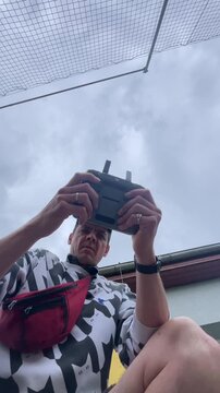 low angle view of adult male holding drone remote control outdoors under overcast sky, fingers on sticks, with focused posture and visible rings on hand in open air