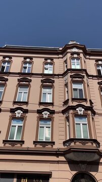 low-angle motion shot of ornate multi-story masonry facade showing decorative window surrounds, sculpted keystones, cornices, and central projecting corner bay stone