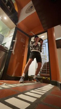 young adult photographer stands in open doorway, shifting weight and lowering camera after shooting, with warm indoor light, reflective surfaces, and candid urban