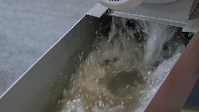 Close up: fast water flow with recycled plastic granules, pellets for cooling the plastic material - part of plastic pelletizer recycling machine. Waste reduction, sustainable, and filtration concept