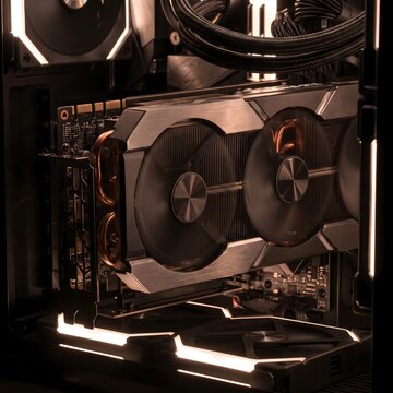 A high-performance graphics card installed inside a desktop computer case, with multiple cooling fans and a large heatsink visible. The dark interior and warm illumination highlight the GPU's cooling 