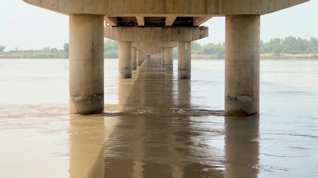 view of a wide river flowing peacefully beneath a sturdy bridge in a scenic rural landscape. 4k video