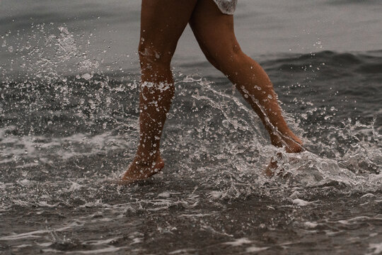 Walking in the shallow water on a beach during dusk. A person walks along the shore where the waves meet the sand at sunset.