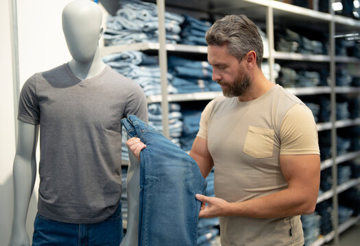 Mature Man shopping elegant clothes. Consumer examines new clothing section. A stylish customer tries on fashionable clothes. Shopper purchases trendy clothes. Trendy fashion clothes market.