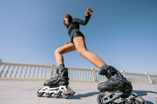 Athletic sporty woman performing a dynamic roller skating move on a sunny promenade, low angle view