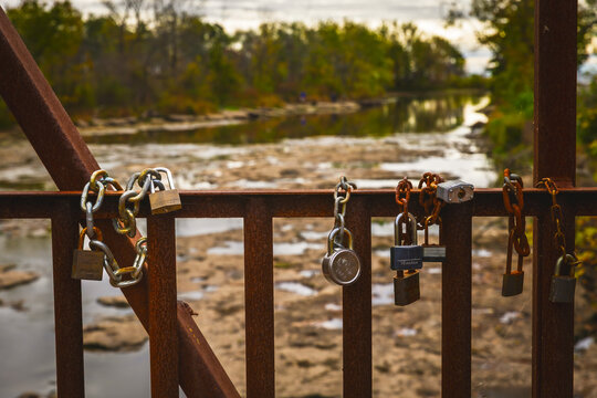Rusting love padlocks and chains on a steel bridge railing above a rocky river, Ontario, Canada.