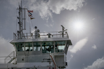 Navigation bridge of a modern vessel. Ship complete with control windows, communication antennas, radar scanner, signal flags flying under a cloudy sky with the sun shining bright.  © Jacek