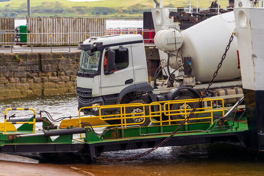 Concrete mixer truck on a ferry loading ramp leaves open car deck via hydraulic  bow ramp at a coastal slipway.  A  a roll-on/roll-off ferry near a stone pier. A modern double-ended hybrid ferry. 