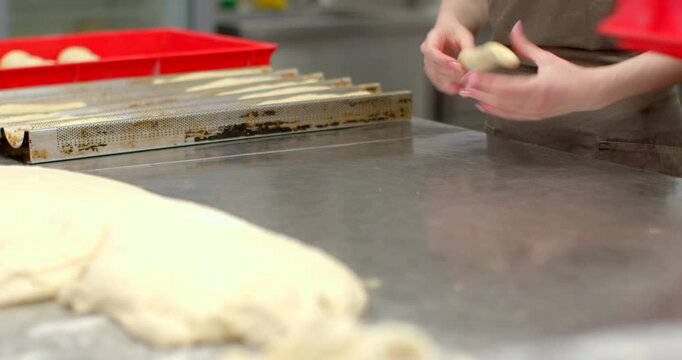 bakers shaping and handling raw dough on reflective stainless steel worktable in commercial bakery, visible actions include pressing, rolling, and reaching for red