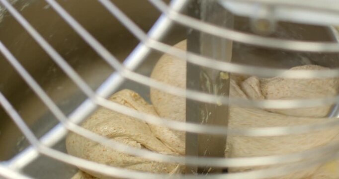 close-up view of wholegrain dough folding and consolidating around central metal paddle inside stainless steel commercial mixer, captured through protective wire