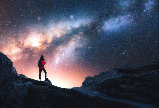 Glowing Milky Way and woman on mountain peak at starry night. Dolomites, Italy. Galaxy. Space landscape with silhouette of a girl, rocks, sky with bright stars. Milky Way and hiker. Nightscape