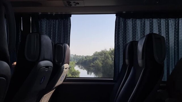 dim passenger coach interior with dark upholstered high-backed seats and patterned deep-blue curtains partially drawn to reveal rectangular window, strong daylight