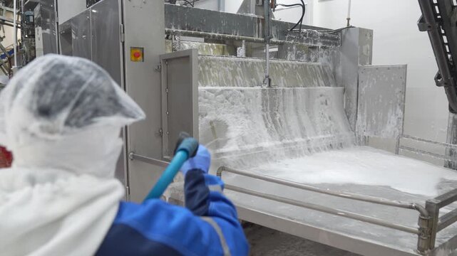 Worker using a high-pressure hose to wash industrial food processing equipment
