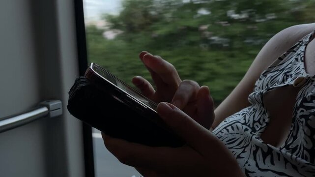 close-up of passenger hands holding smartphone in protective case while tapping screen beside vehicle window, patterned sleeveless dress and partial torso visible