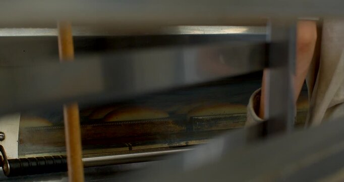 mid-bake scene showing multiple bread loaves traveling on conveyor through commercial oven, tops developing golden-brown crusts and domed shapes, warm interior bread