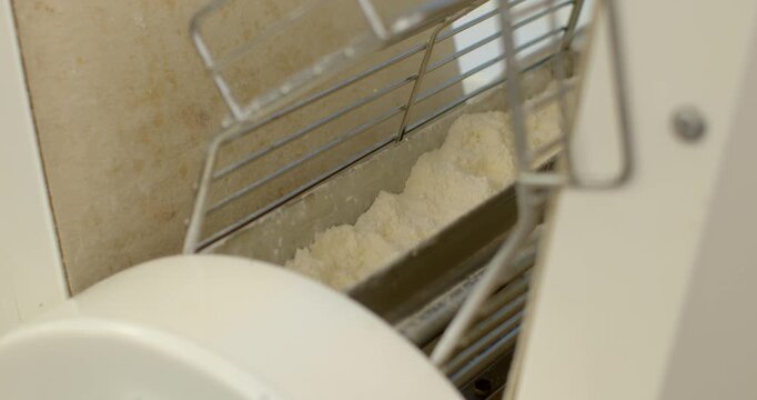 close-up view of powdery off-white flour settled inside stainless steel chute of bakery hopper, visible beneath protective wire guard and pale plastic housing bakery