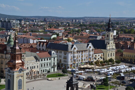 Aerial view of Oradea, Romania, featuring the historic city center, colorful rooftops, elegant architecture, Crișul Repede River, and distant Apuseni Mountains under a clear sky.