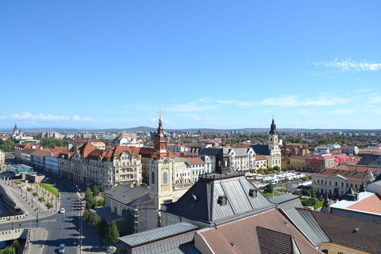 Aerial view of Oradea, Romania, featuring the historic city center, colorful rooftops, elegant architecture, Crișul Repede River, and distant Apuseni Mountains under a clear sky.