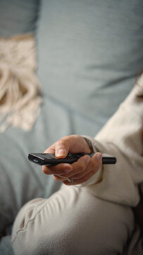 Close-up of an anonymous woman&rsquo;s hand using a television remote while sitting on a sofa, highlighting home entertainment, media selection, technology, and everyday leisure.