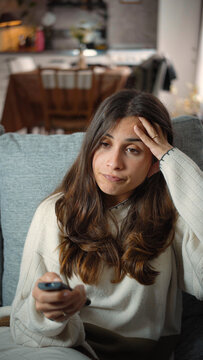 Young Latina woman sitting frustrated on her sofa while watching television, portraying media dissatisfaction, boredom, emotional tension, and everyday home life.