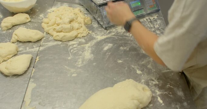 close-up view of baker preparing unbaked dough portions at floured stainless steel workstation, hands placing and shaping dough into round metal molds on baking