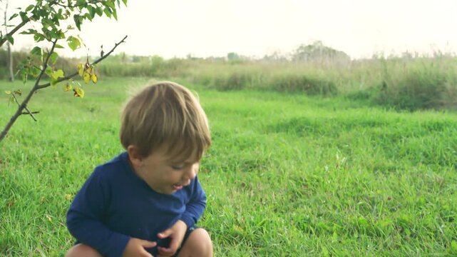 Toddler crouching down to examine a wild mushroom growing in the grass