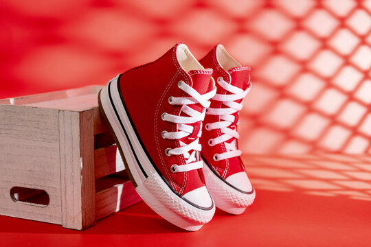 Red Converse sneakers lean against a crate beneath patterned window shadows.