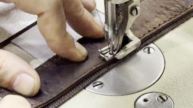 Close-up view of a craftsperson using an industrial sewing machine to stitch a durable leather belt with reinforced fabric webbing. The image highlights precision workmanship, leather craftsmanship