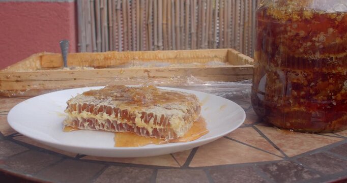 close-up motion on honeycomb slice and amber honey jar, honey glistening with subtle flow while set on mosaic patio table for natural food styling