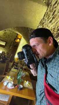 a man is holding a camera and looking through it in an indoor setting with stone walls, creating a neutral to focused first-person perspective from the man's point.