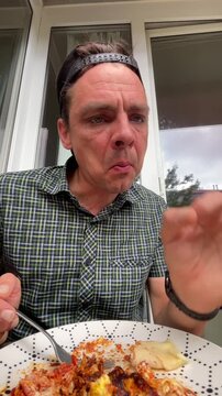 close-up of man eating during casual home dining on balcony, holding fork and torn bread while leaning forward and gesturing, natural daylight and lifestyle mood