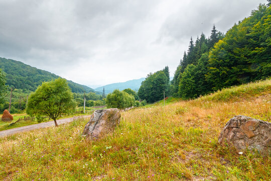 rural landscape. fence near road through field and forest to the high mountains. countryside scenery of ukraine in summer with overcast sky